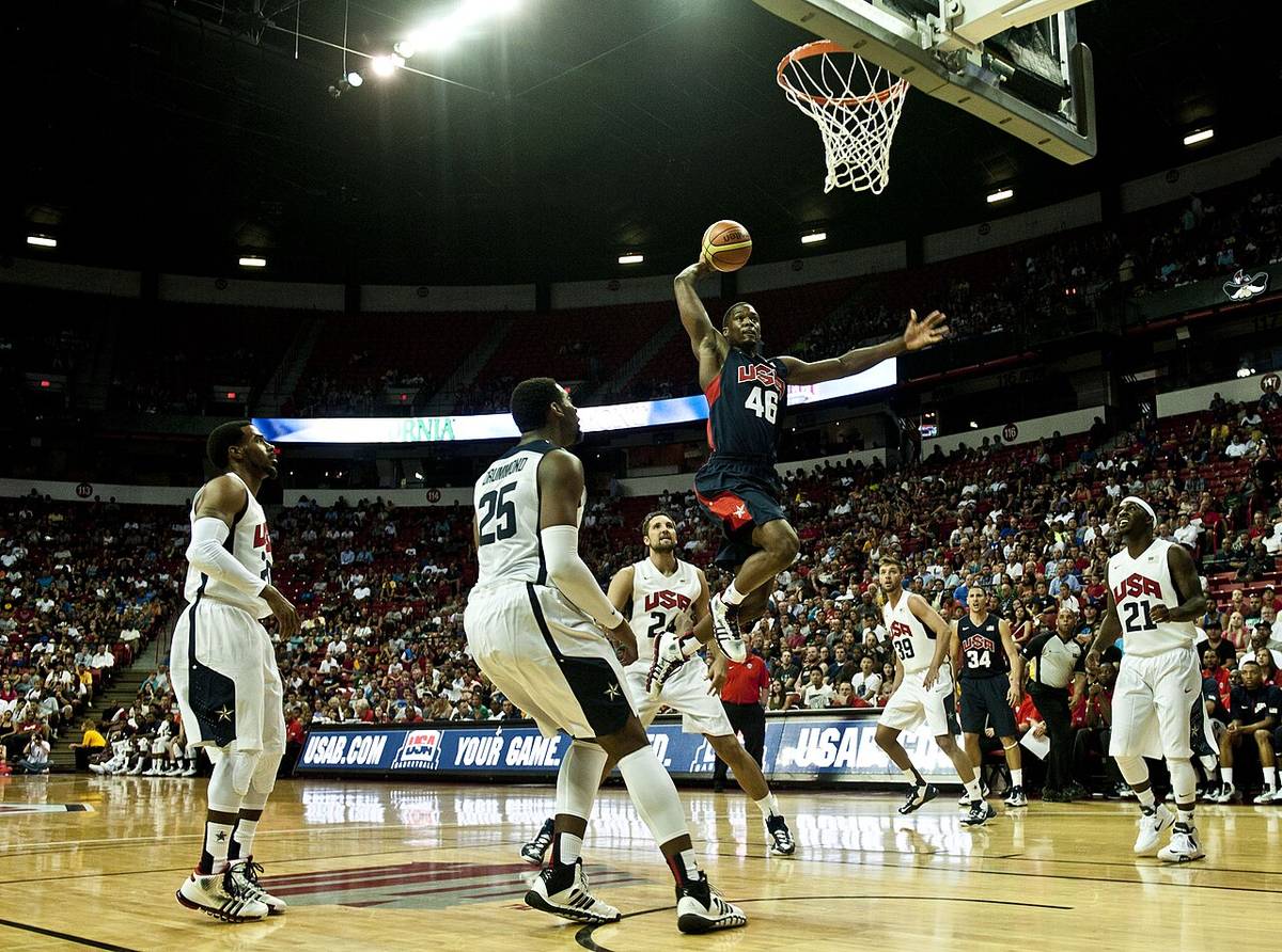 Basketball players contest a dunk in front of packed stands